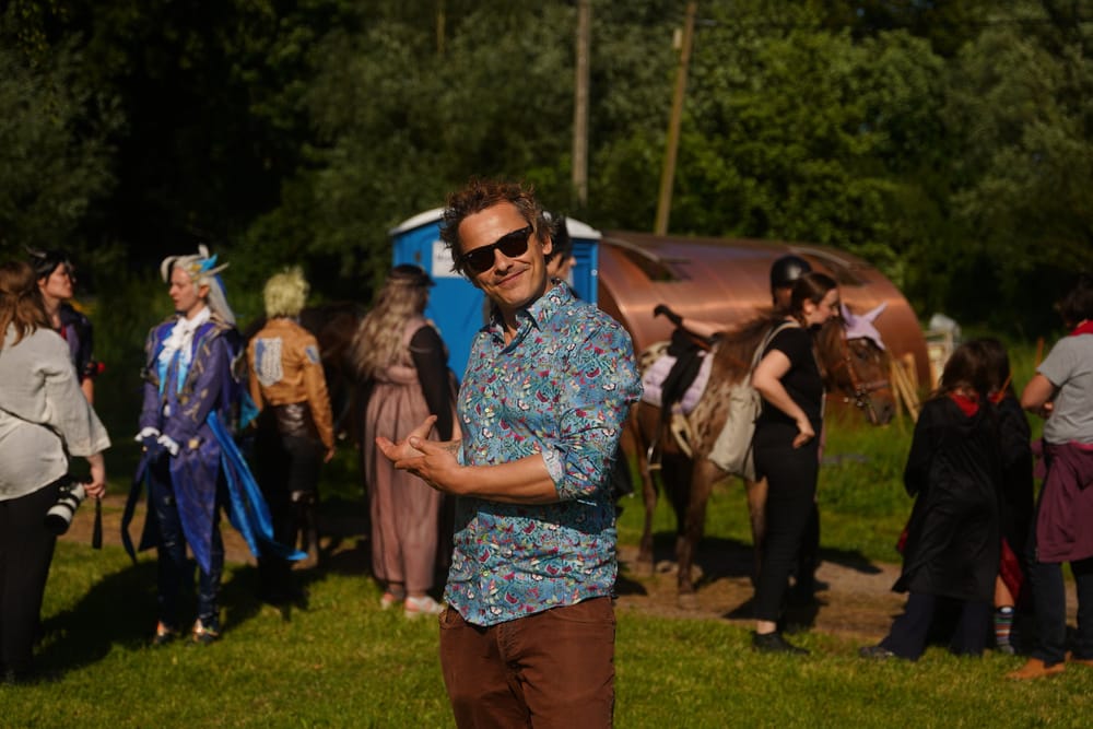 Charismatischer Mann zeigt auf den Hintgergrund mit Menschen und Dixie-Klo.